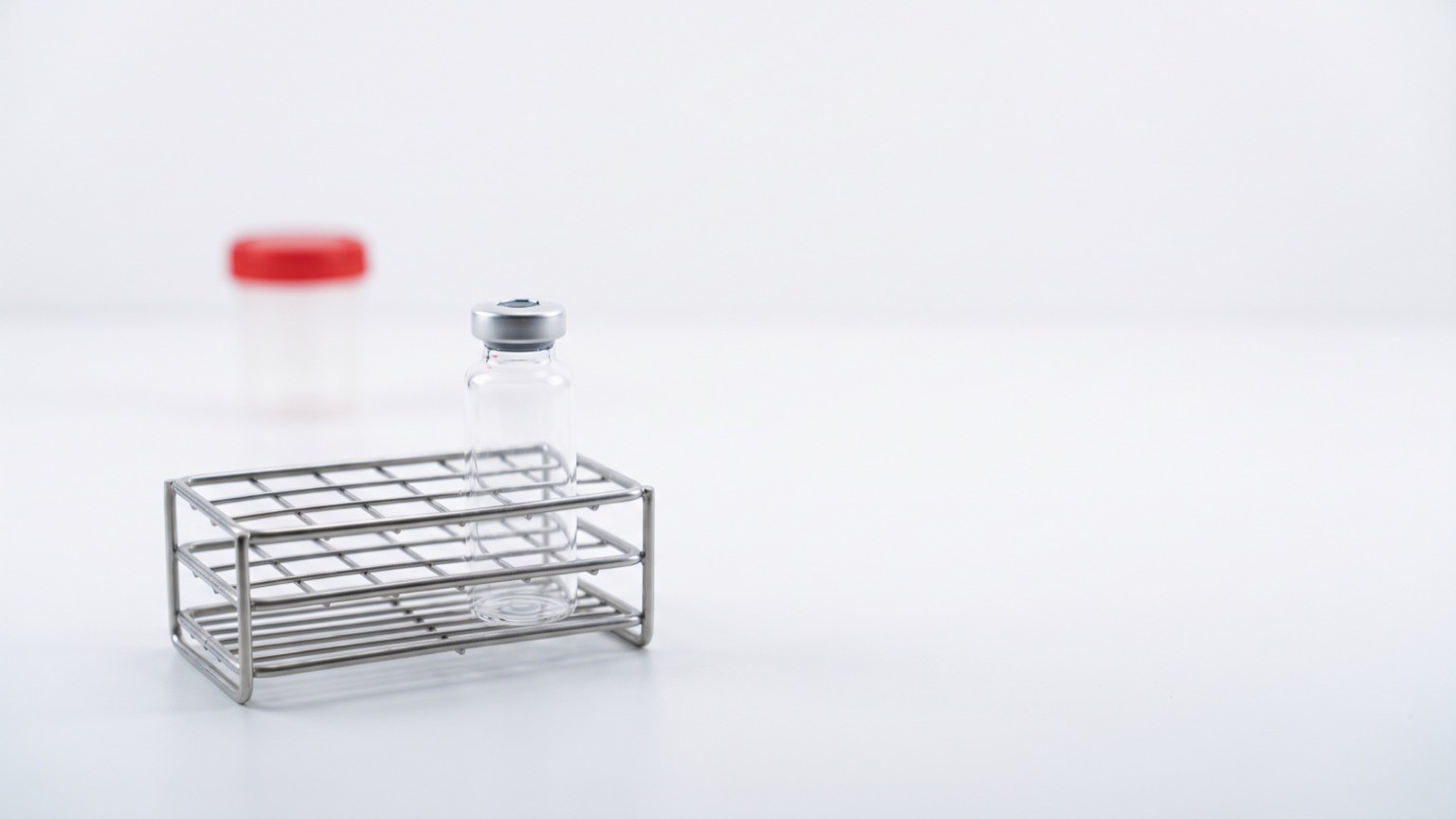 Vial de investigación sin etiqueta en gradilla de acero sobre mesa de laboratorio blanca