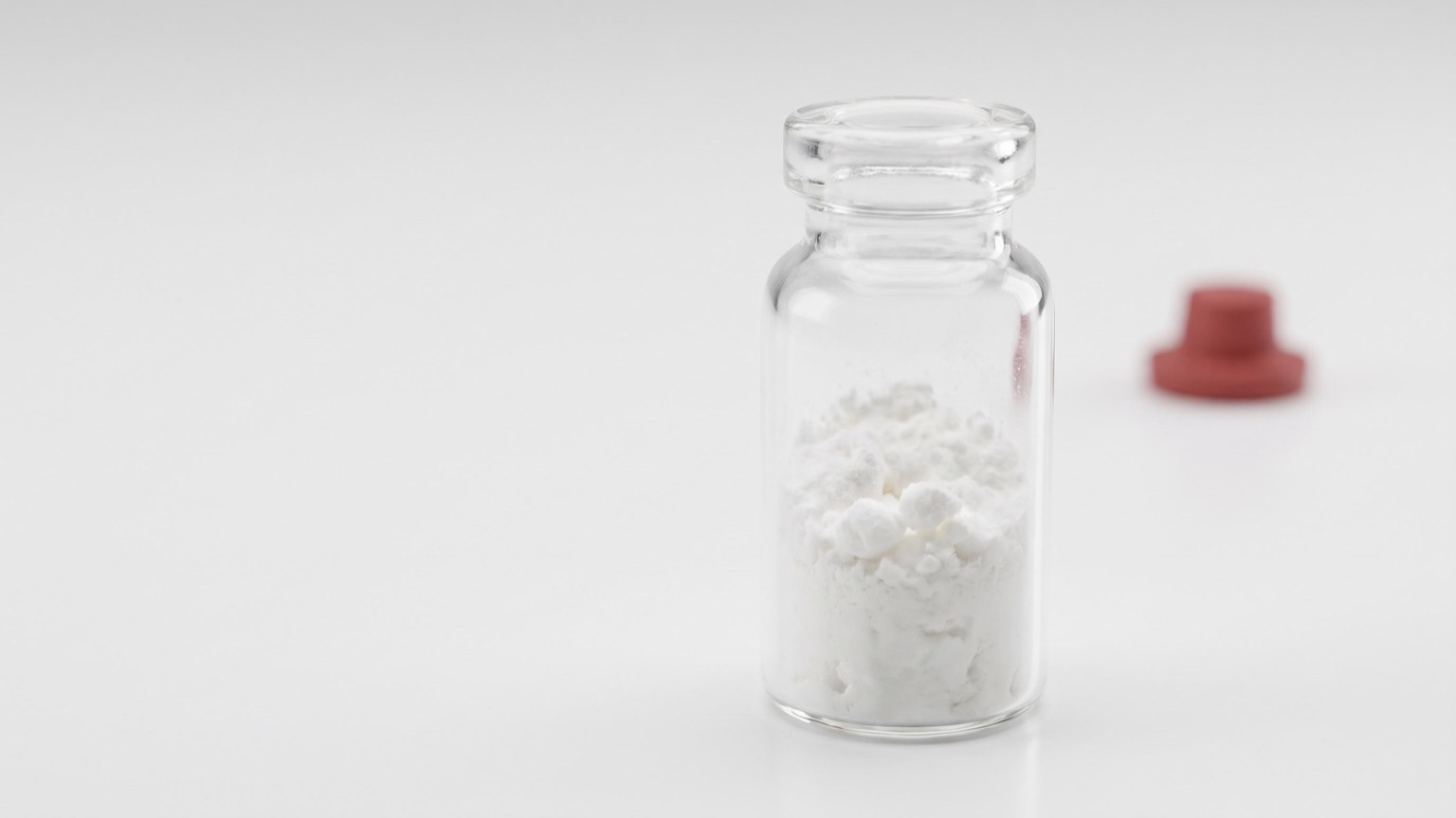 Macro de vial de vidrio con péptido liofilizado en superficie de laboratorio blanca
