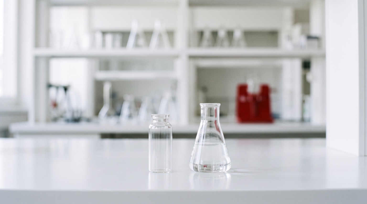 Vial de investigación sin etiqueta junto a matraz de vidrio en laboratorio blanco